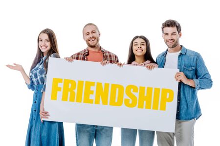 happy multicultural friends holding placard with yellow friendship lettering isolated on white