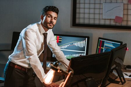 bi-racial trader standing near computers and looking at camera