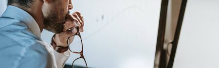 panoramic shot of bi-racial trader looking at computer and holding glasses