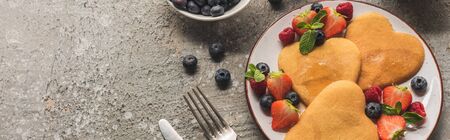top view of heart shaped pancakes with berries on grey concrete surface with cutlery, panoramic shotの写真素材
