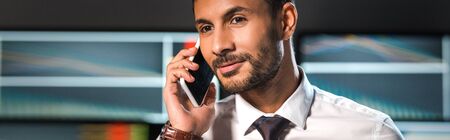 panoramic shot of smiling bi-racial trader talking on smartphone