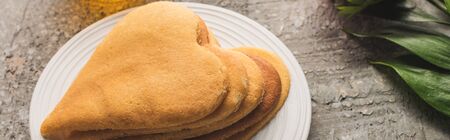 delicious heart shaped pancakes on plate near plant on grey concrete surface, panoramic shot