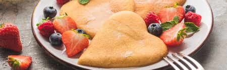 delicious heart shaped pancakes with berries on plate with fork on grey concrete surface, panoramic shotの写真素材