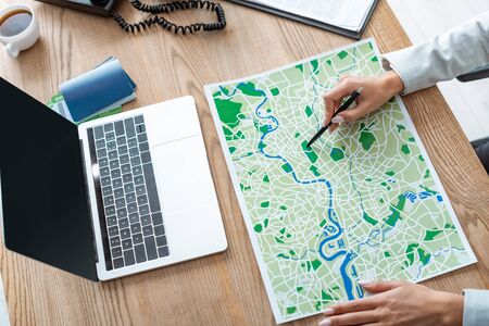 cropped view of travel agent pointing with pen at map on wooden deskの写真素材
