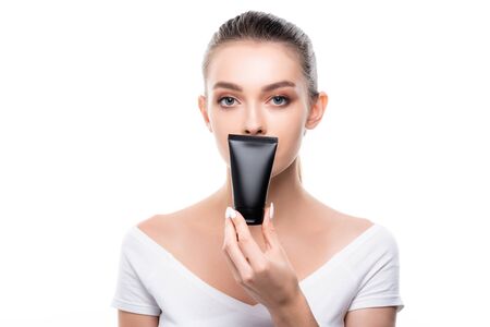 beautiful girl looking at camera while holding tube with hand cream isolated on whiteの写真素材