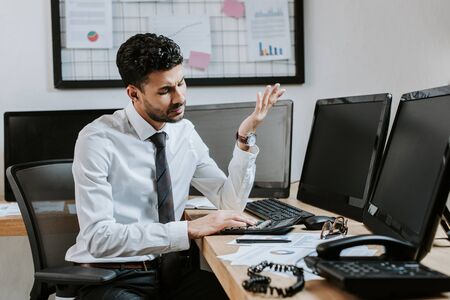 bi-racial trader using calculator and sitting at table in office