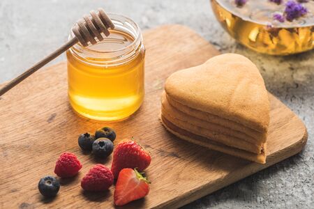 delicious heart shaped pancakes with berries on wooden board with honey