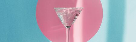 gin and tonic in martini glass in pink circle on blue background in sunlight, panoramic shot