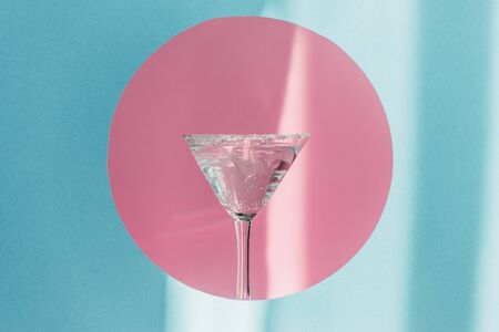 gin and tonic in martini glass in pink circle on blue background in sunlightの写真素材