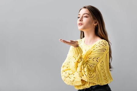 pretty girl in yellow sweater showing blowing kiss isolated on greyの写真素材