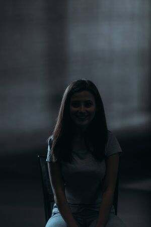 young woman smiling at camera while sitting on dark background with lighting