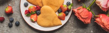 top view of heart shaped pancakes with berries on grey concrete surface near roses, panoramic shotの写真素材