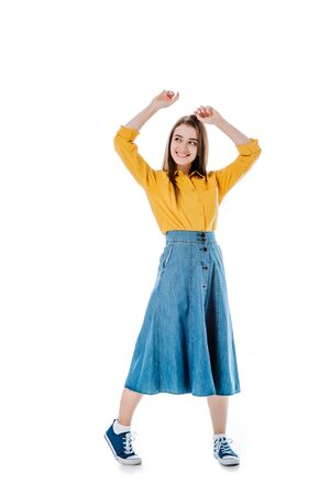 full length view of happy attractive girl dancing with hands in air and looking away isolated on whiteの写真素材