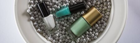 top view of assorted nail polish in bottles on plate with grey decorative beads, panoramic shotの写真素材
