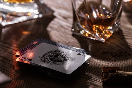 KYIV, UKRAINE - NOVEMBER 7, 2019: Glass of brandy with cigar and playing cards on wooden table