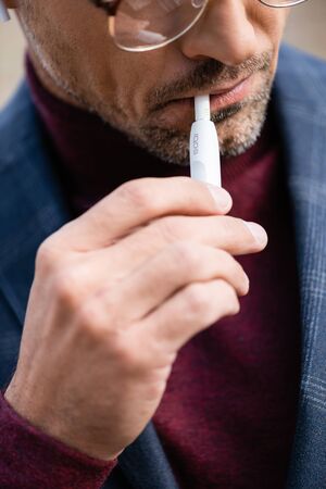 KYIV, UKRAINE - OCTOBER 11, 2019: Cropped view of businessman in eyeglasses smoking iqos outdoorsのeditorial素材