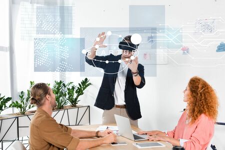 smiling businessman with vr headset gesturing in office near colleagues and startup illustration