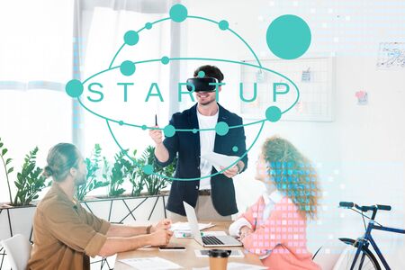 smiling businessman with vr headset in office near colleagues and startup illustrationの写真素材