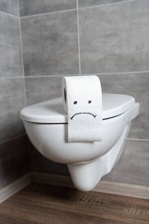 Sad emoticon on toilet paper on ceramic toilet bowl in bathroom