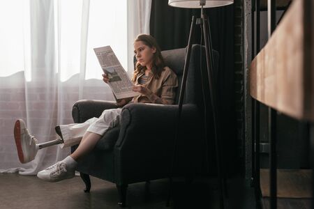 Beautiful girl with prosthetic leg reading newspaper at home