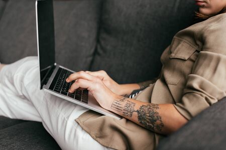 Cropped view of young woman using laptop on sofaの写真素材