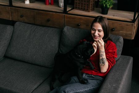 Smiling girl playing with pug on sofa in living roomの写真素材