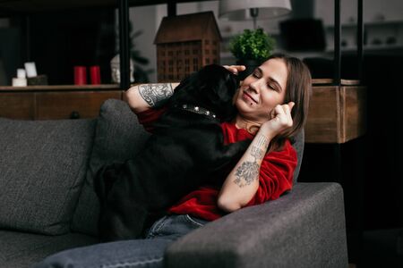 Beautiful girl with amputated leg playing with pug dog on sofa at homeの写真素材