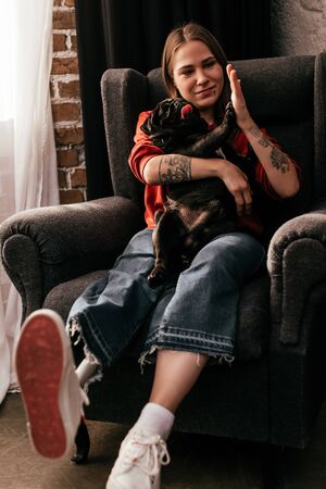 Smiling girl with prosthetic leg high five to pug dog in armchair in living roomの写真素材