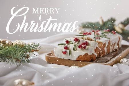 selective focus of traditional Christmas cake with cranberry on wooden board near baubles and pine needles isolated on grey with Merry Christmas illustrationの写真素材