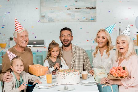 happy family sitting at kitchen table near birthday cake under falling confettiの写真素材