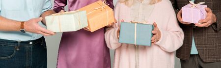 cropped view of senior parents with adult son and daughter holding gift boxes isolated on grey, panoramic shotの写真素材