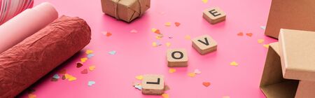 valentines confetti, wrapping paper, gift boxes, love lettering on wooden cubes on pink background, panoramic shotの写真素材