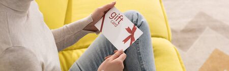 Cropped view of young woman holding gift card on sofa, panoramic shotの写真素材