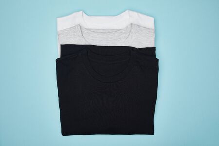 top view of blank basic black, white and grey t-shirts isolated on blue