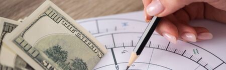 Cropped view of astrologer drawing natal chart with dollar banknotes on table, panoramic shot