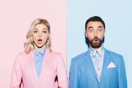 shocked woman and handsome man looking at camera on pink and blue backgroundの写真素材