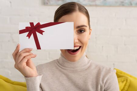 Attractive exited girl covering face with gift card and looking at camera
