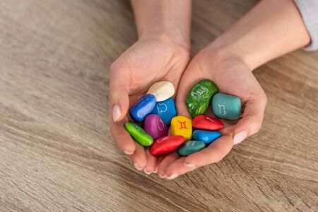 Cropped view of woman holding in hands colorful stones with zodiac signs at wooden tableの写真素材