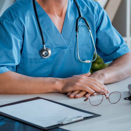 cropped view of doctor sitting with clenched hands in clinicの写真素材