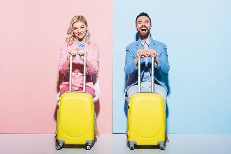 smiling woman and handsome man holding travel bags on pink and blue backgroundの写真素材