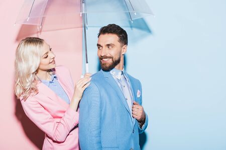 smiling woman with umbrella looking at handsome man on pink and blue backgroundの写真素材