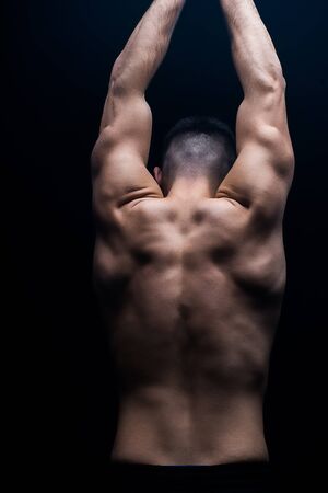back view of sexy muscular bodybuilder with bare torso posing isolated on black