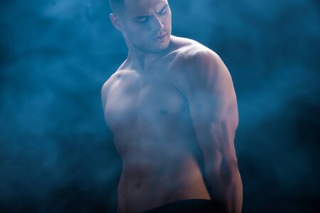 sexy muscular bodybuilder with bare torso on black background with smokeの写真素材