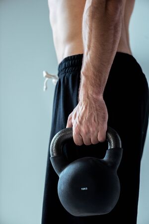 partial view of sexy muscular bodybuilder exercising with kettlebell isolated on grey