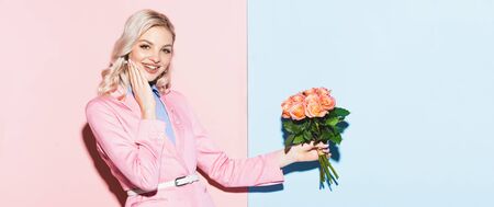 panoramic shot of smiling woman holding bouquet on pink and blue backgroundの写真素材