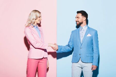 smiling woman and handsome man shaking hands on pink and blue backgroundの写真素材
