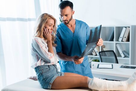 handsome orthopedist and shocked woman looking at x-rayの写真素材