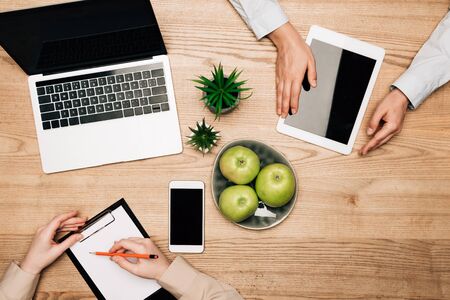 Top view of colleagues with digital devices and clipboard on table, cropped viewの写真素材
