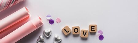 top view of silver hearts, wrapping paper and cubes with love lettering on white background,...