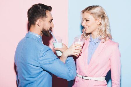 attractive woman and smiling man drinking cocktails on pink and blue backgroundの写真素材